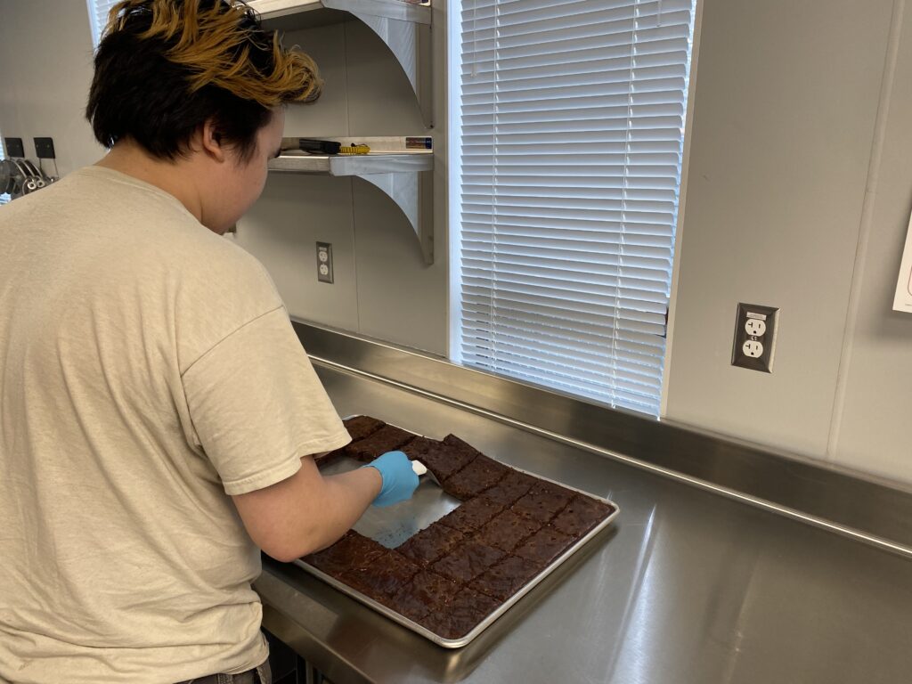 Young person cuts a tray of baked goods