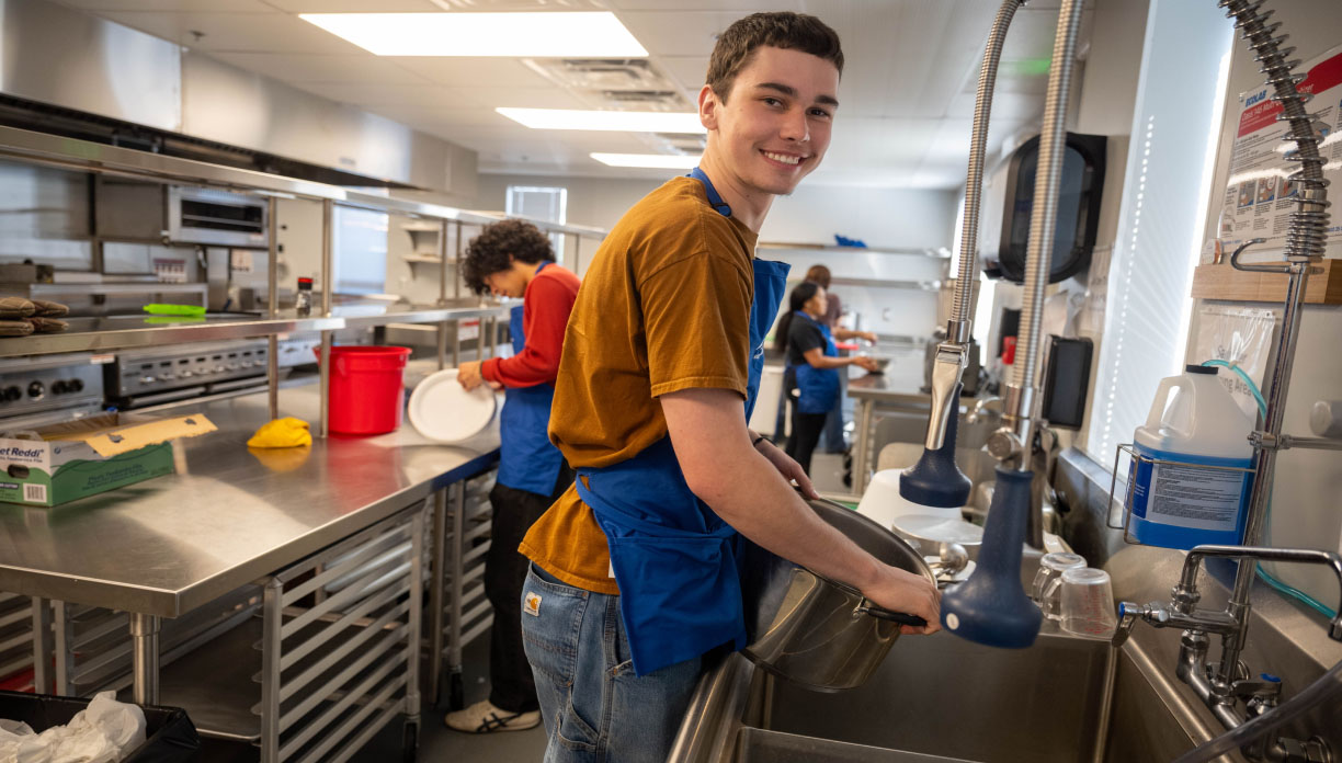 A young man in a commercial chicken washing dishes