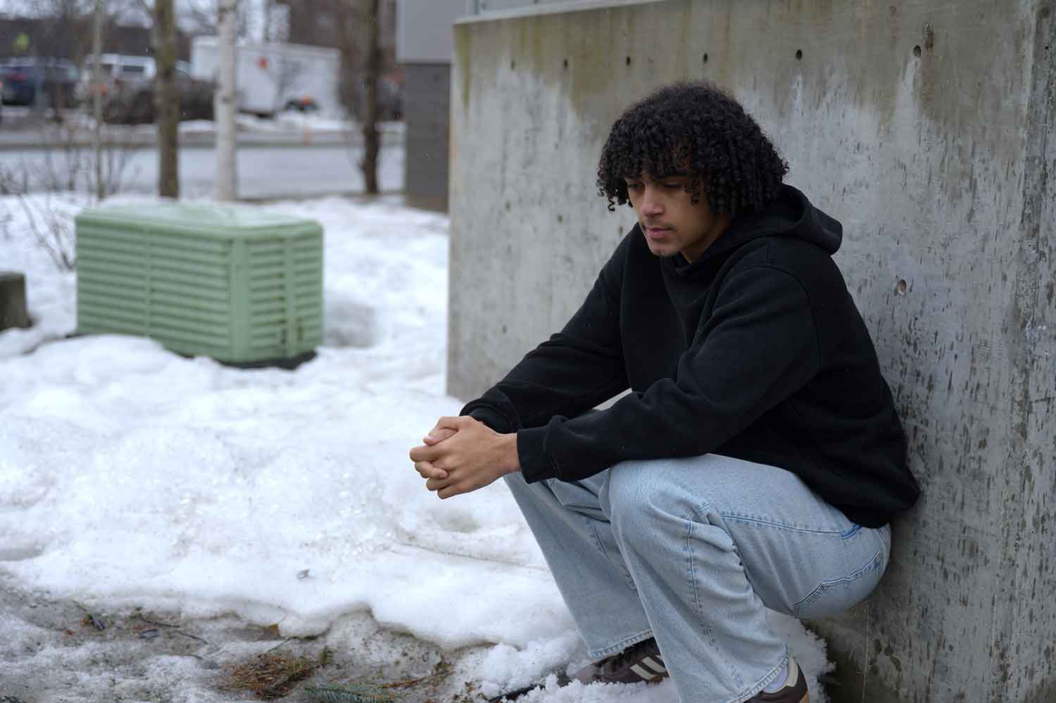 A young man crouching in the snow in sneakers without any gloves.